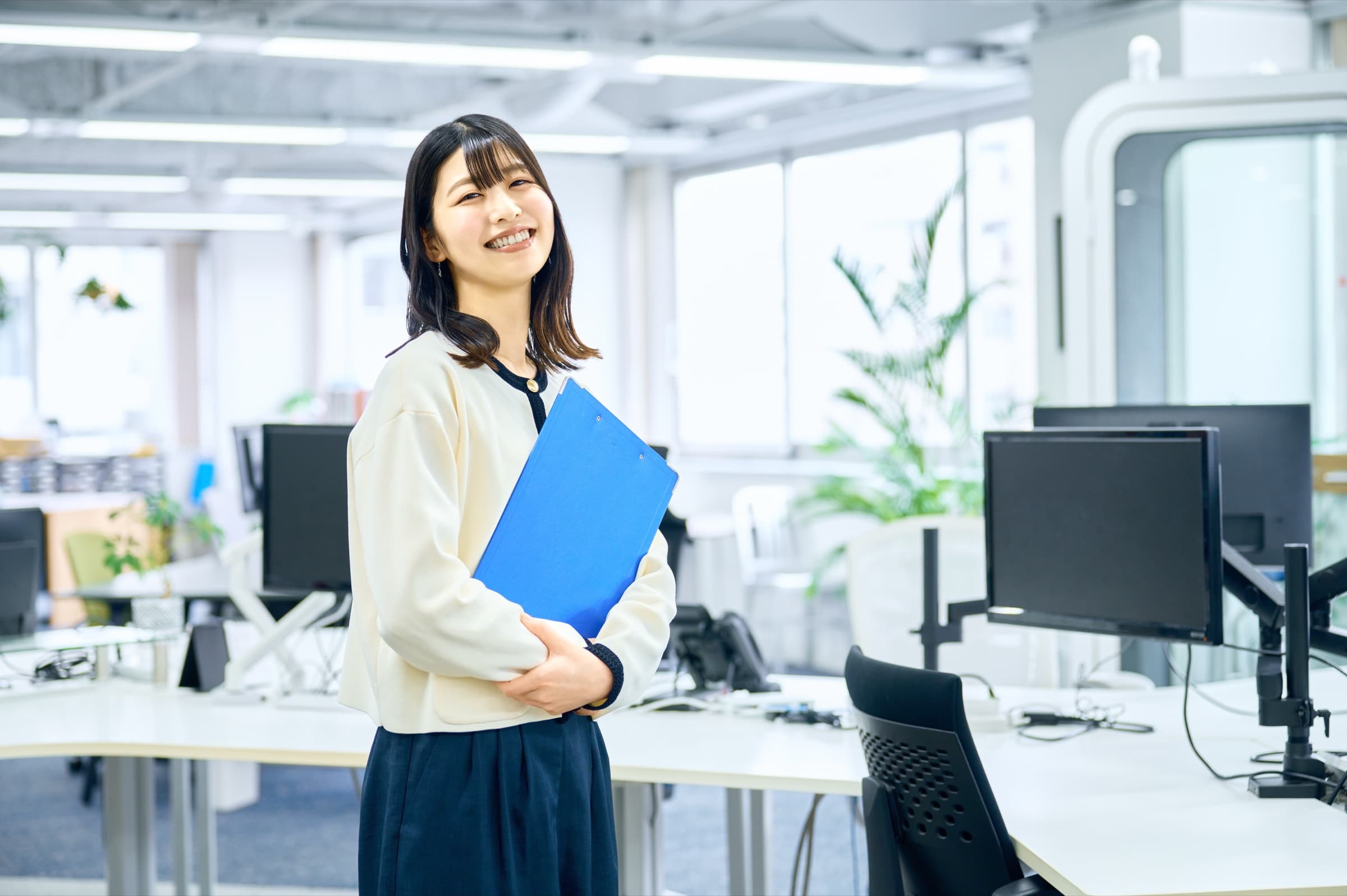 青いファイルを持った女性がオフィスに立っている